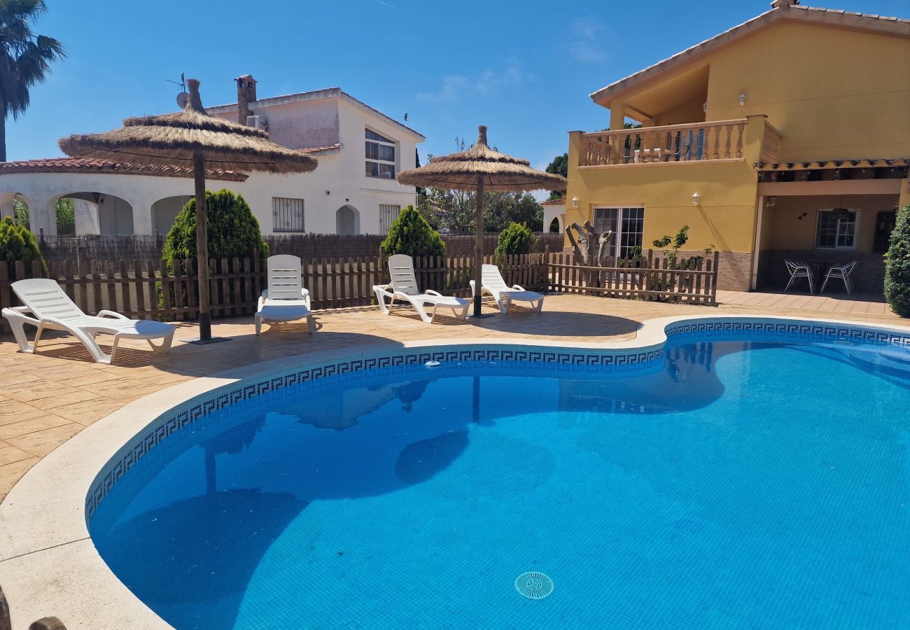 Blick über den riesigen Pool mit fest montierten Strohsonnenschirmen auf das Ferienhaus Eva.